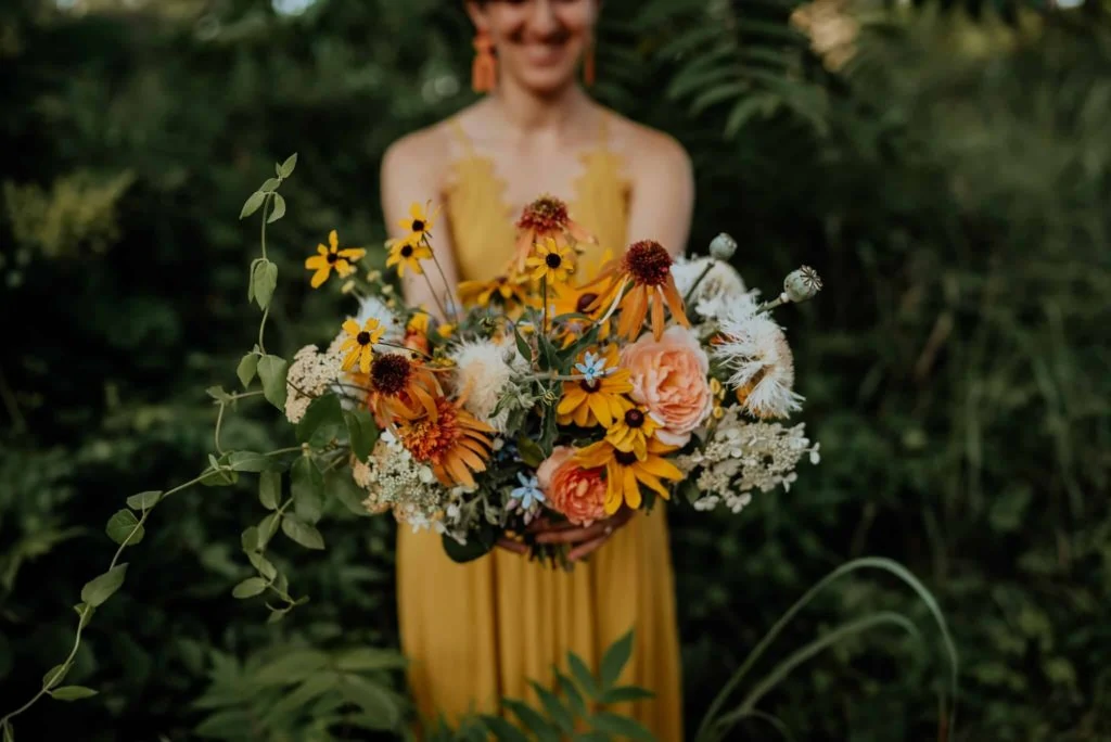 A bride in a yellow wedding dress holds out a lush wedding bouquet.