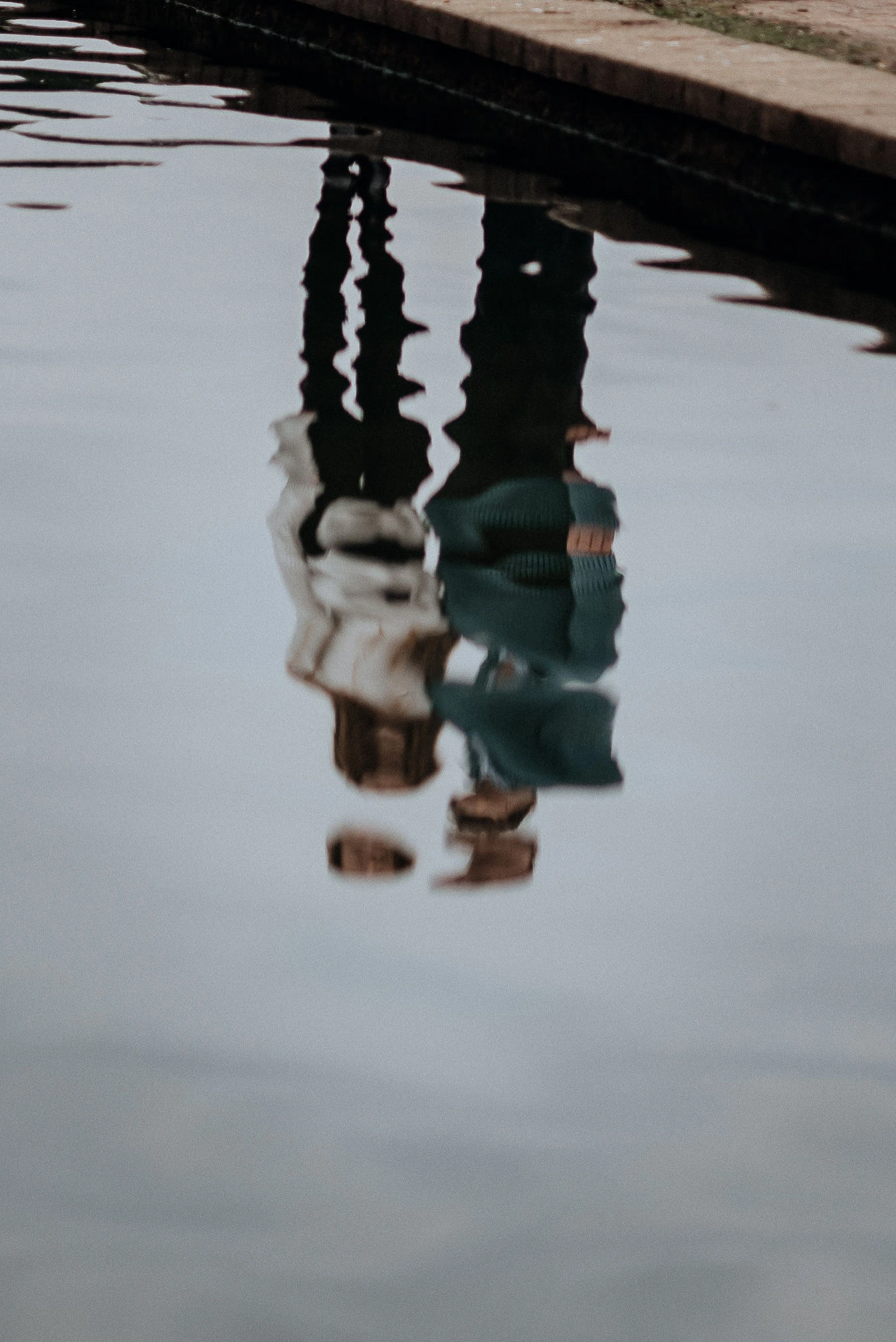 A wavy reflection in the water of a couple standing on the bank