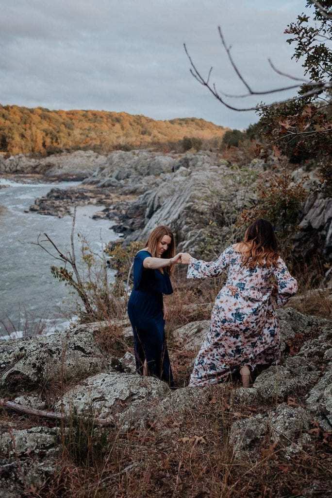 A woman helps her partner climb down a rocky slope at Great Falls Park