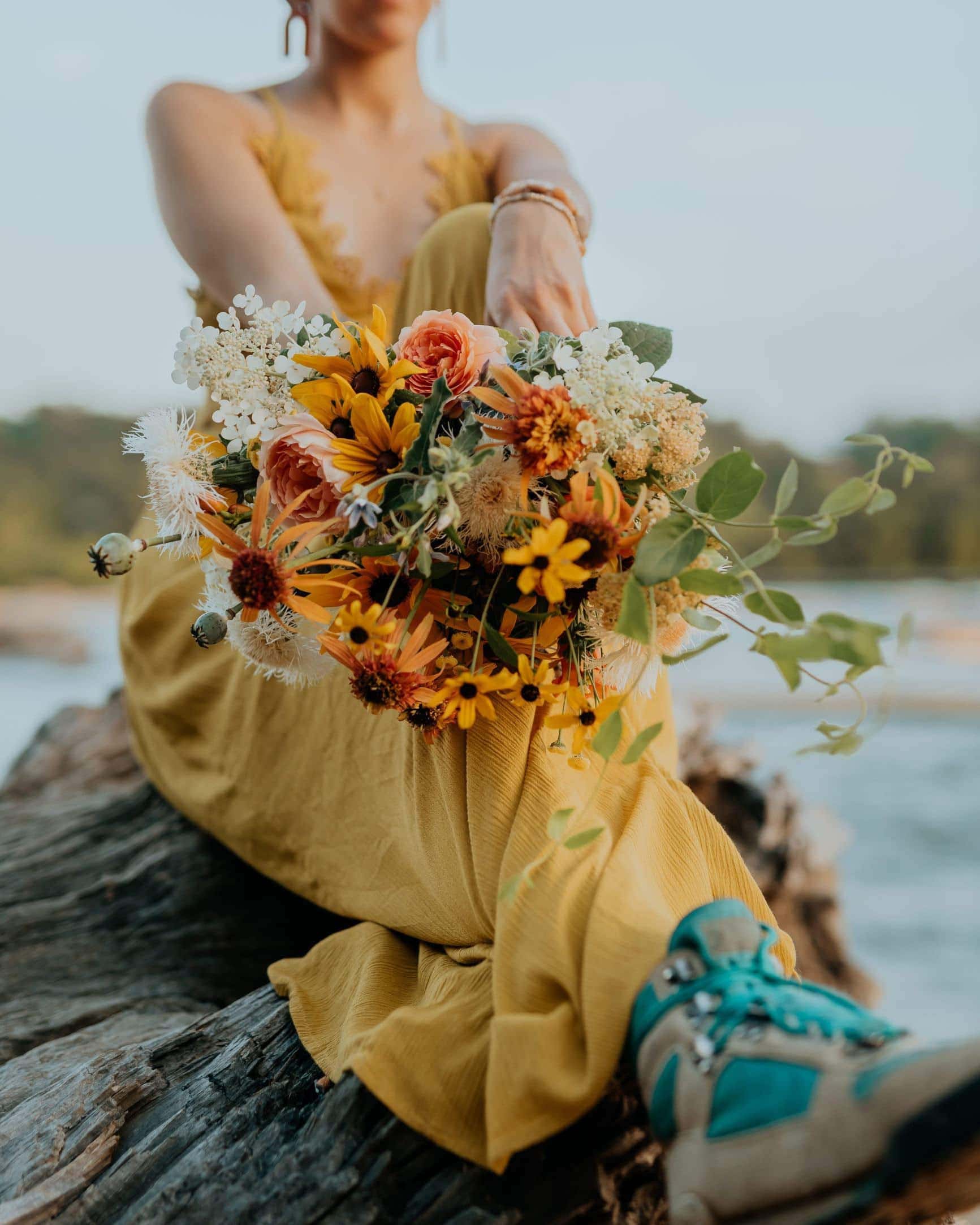 A bride in a yellow dress and vintage hiking boots shows off her bouquet.