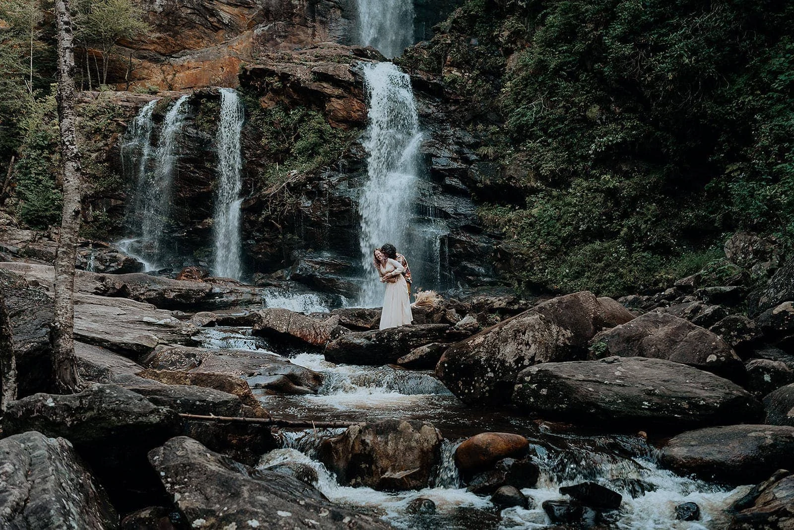 An eloping couple laughs together in front of a large waterfall in North Carolina