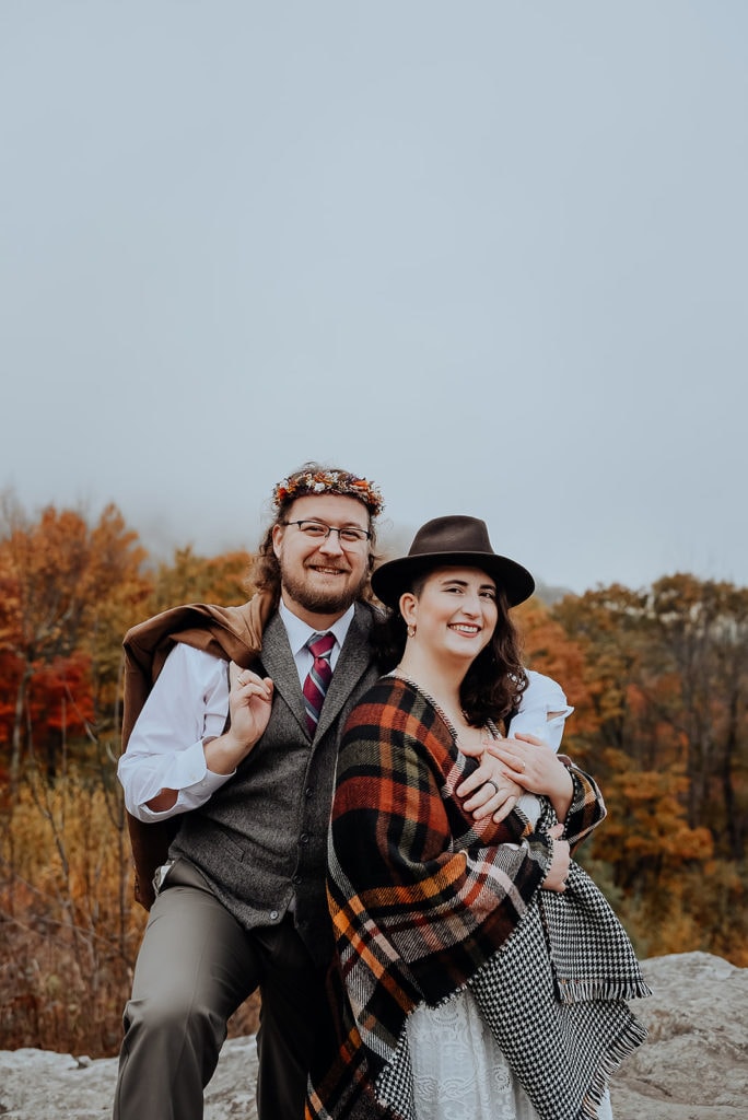 A couple eloping in Shenandoah National park switches hats and smiles in front of fog and fall foliage. 